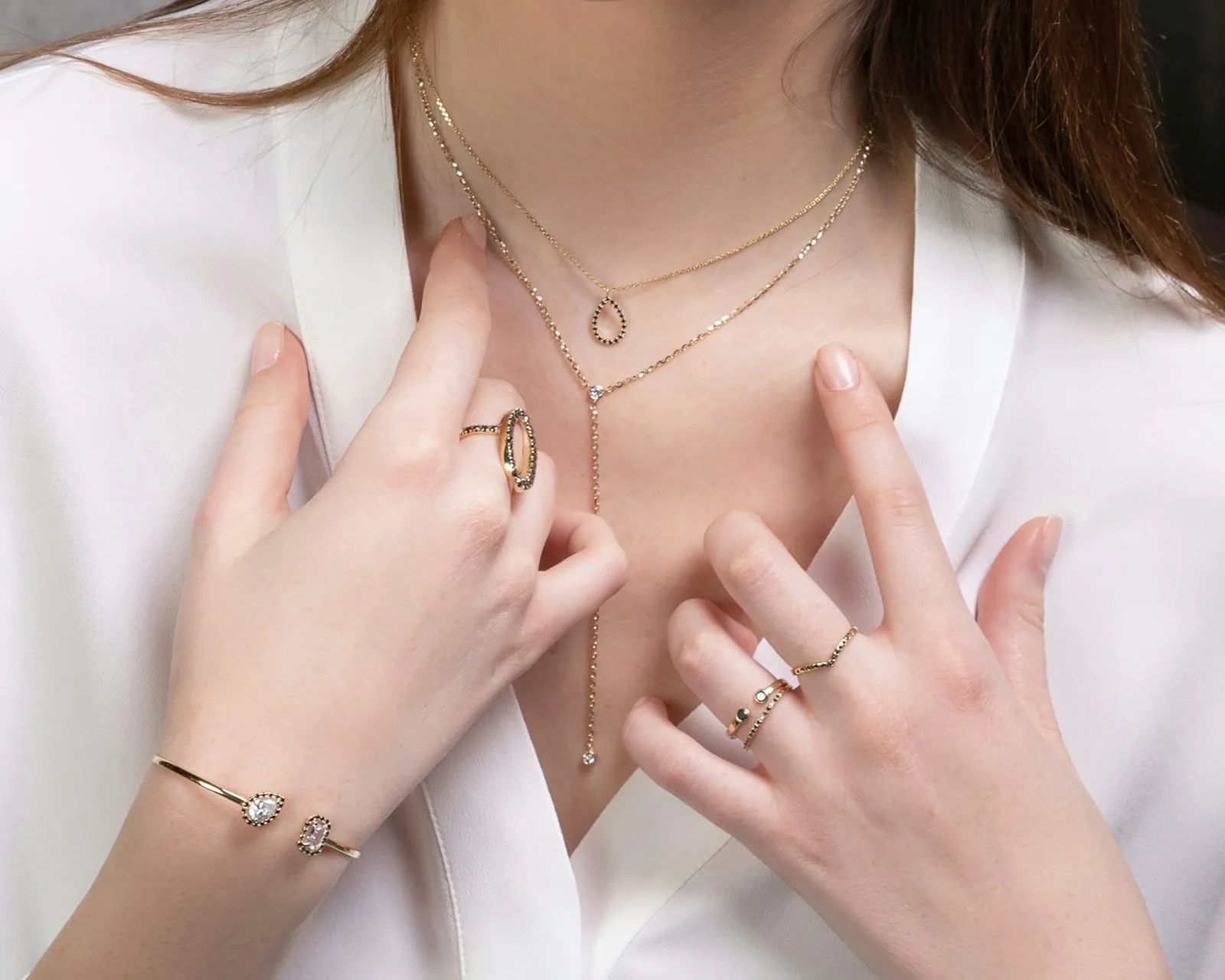 Mujer con collares finos, anillos y pulsera de plata y oro sobre camisa blanca